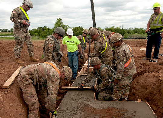 Military service members and County Materials team members working together on a concrete project, fostering teamwork and community connections.