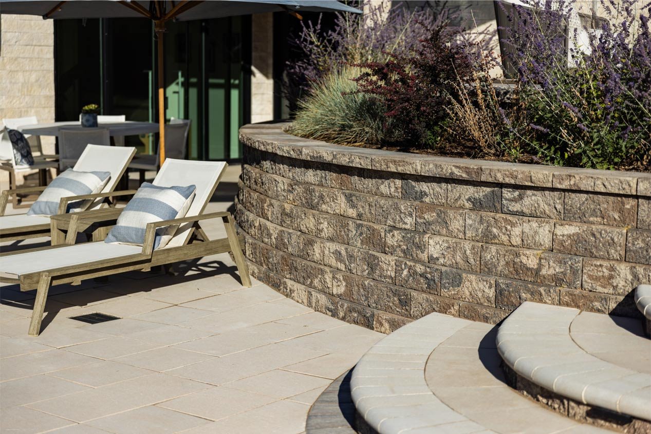 Curved steps lead down to a patio with a curved retaining wall and two lounge chairs.