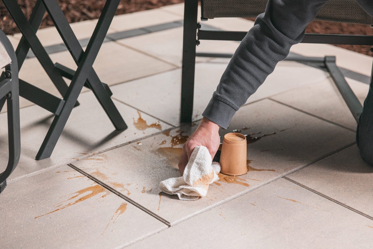 Close-up of someone cleaning spilled coffee off of concrete pavers with Sentinel Sealed Technology using just a clean cloth.