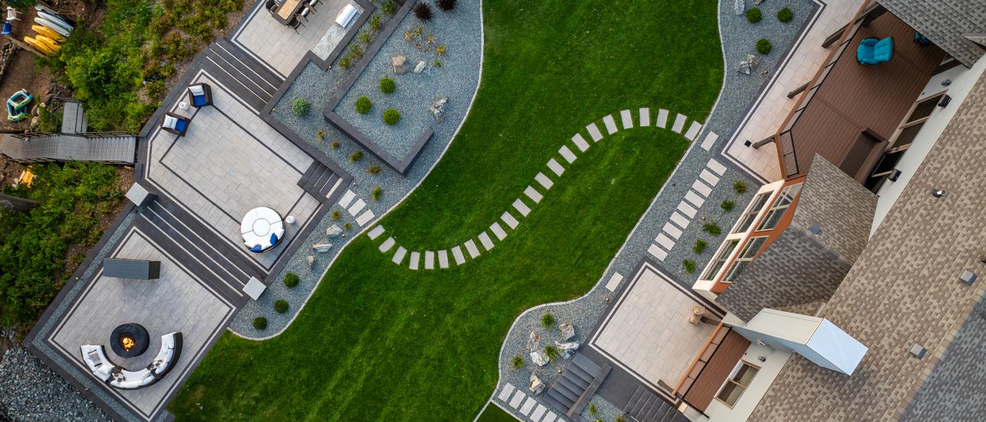 An overhead view of a multi-tier patio with seven gathering and entertaining areas, including a dining and grill patio, a seating patio surrounding a fire feature, a patio overlooking the river, and a patio next to a putting green.